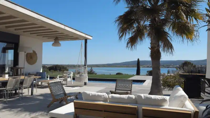Vu d'une terrasse en bois avec jardin en gazon synthétique et une piscine donnant sur l'étang de Thau et Sète.