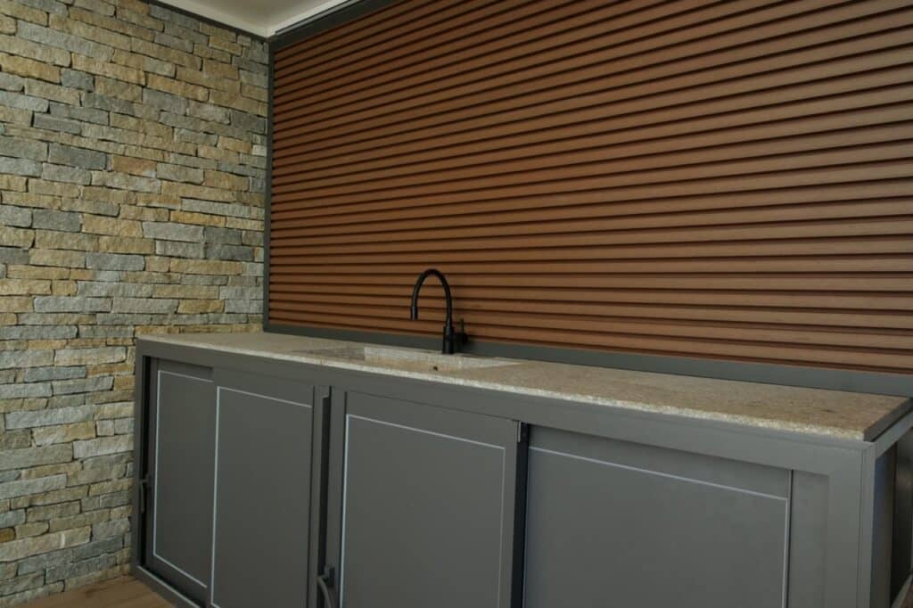 Cuisine d'été en aluminium thermolaqué avec mur en parement pierre et bardage aluminium.