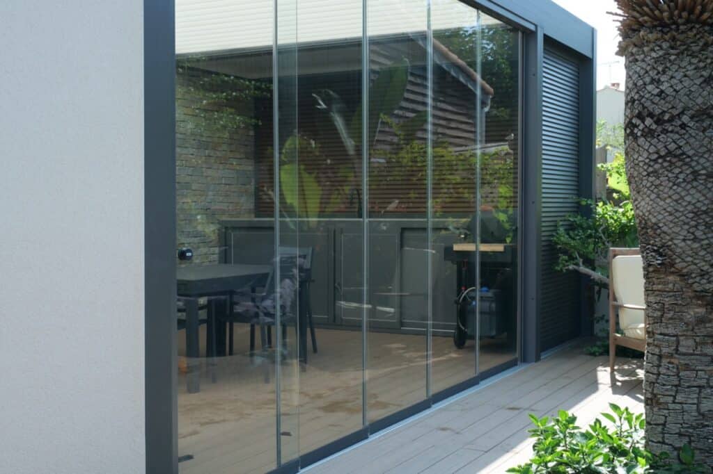Mur de verre ou baie vitré de la marque sunflex. Transition entre cuisine d'été et la terrasse.