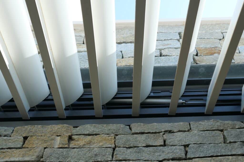 Lames orientables de pergola bioclimatique dans un montant encastré dans un mur.